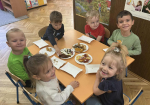 Zdjęcie przedstawia dzieci zajadające różne smakołyki