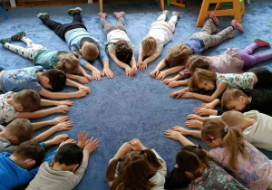Zdjęcie przedstawia dzieci leżące w okręgu podczas ćwiczeń