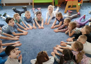 Zdjęcie przedstawia dzieci leżące w okręgu podczas ćwiczeń