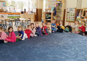 Dzieci siedzące na dywanie, jedno za drugim, tworzące pociąg, masujące plecy