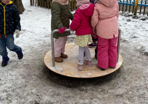 Zdjęcie przedstawia dzieci w ogrodzie przedszkolnym w zimową pogodę