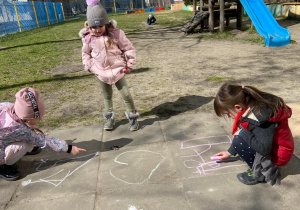 Zdjęcie przedstawia dzieci w trakcie rysowania kredą po chodniku