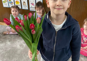 Zdjęcie przedstawia chłopca z bukietem kwiatów